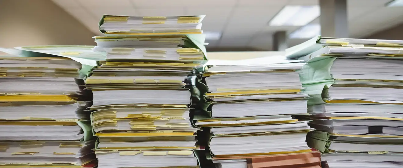 Stacks of paper documents and folders piled on an office desk