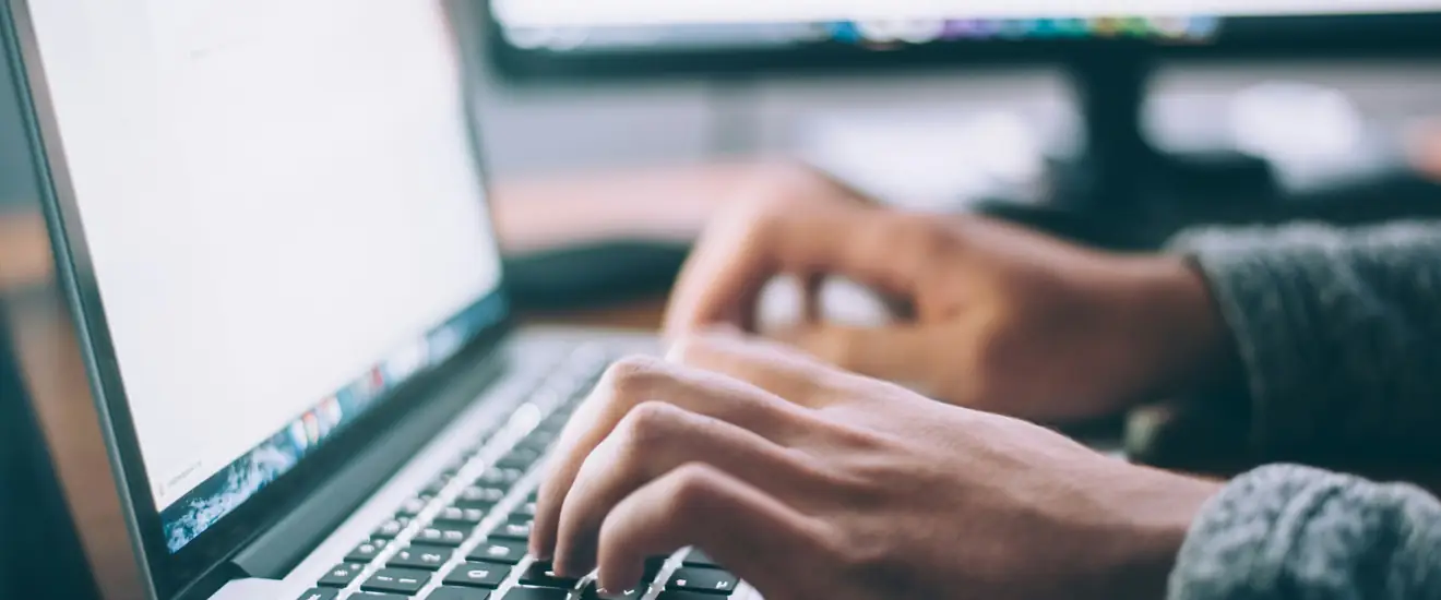 Hands typing on a laptop keyboard, the screen at an oblique angle