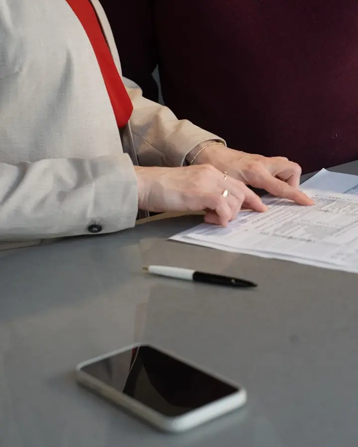 Two people at a table reading through a printed form, a pen and a phone beside it